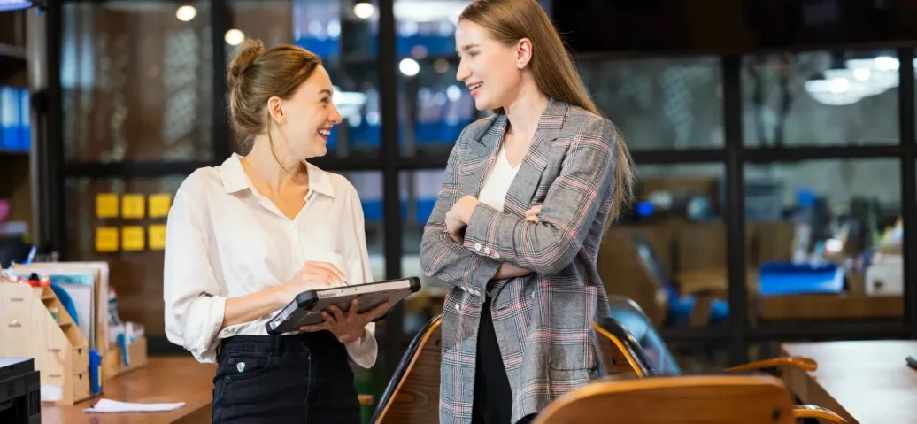 Two professionals in an office setting, one holding a tablet.