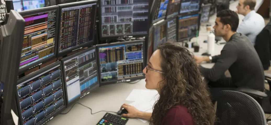 Traders at desks with multiple computer monitors displaying financial data.