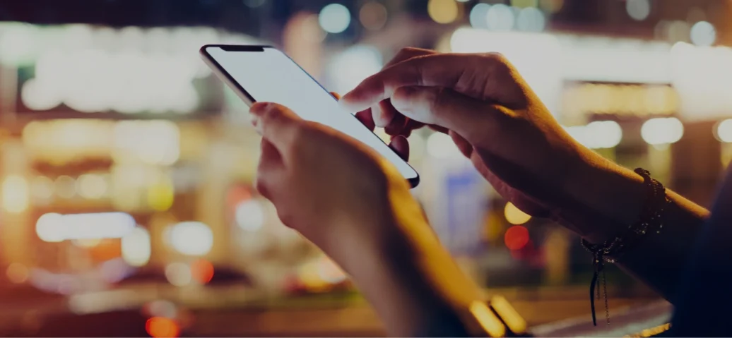 A person holds a cell phone against a cityscape, featuring a fingerprint overlay symbolizing advanced cybersecurity technology.