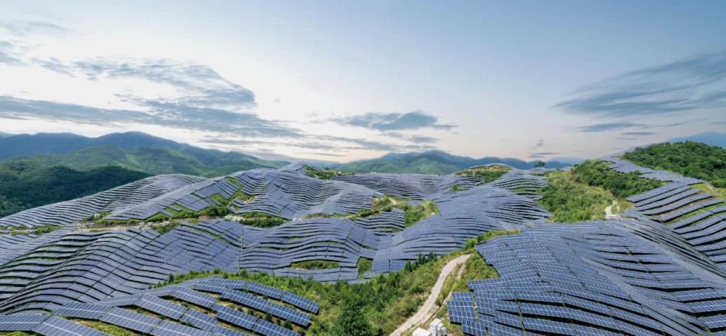 Vast solar panel installation sprawling across hilly terrain under a cloudy sky.