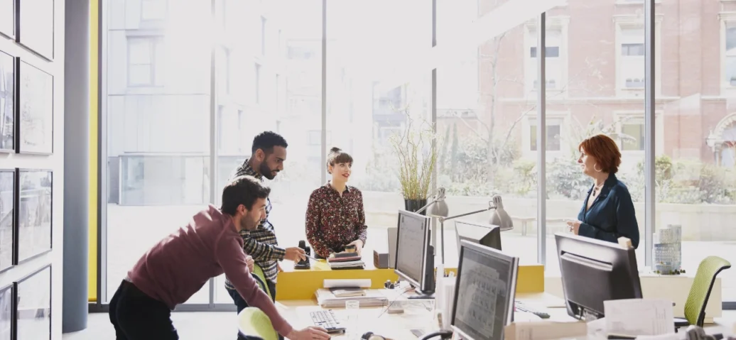 A bright office space with professionals working at desks by large windows.