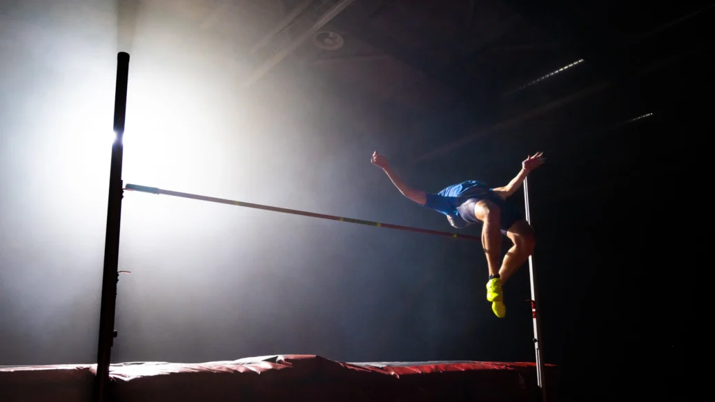 A man leaps over a high jump bar, showcasing athleticism and determination in a dynamic sports moment.