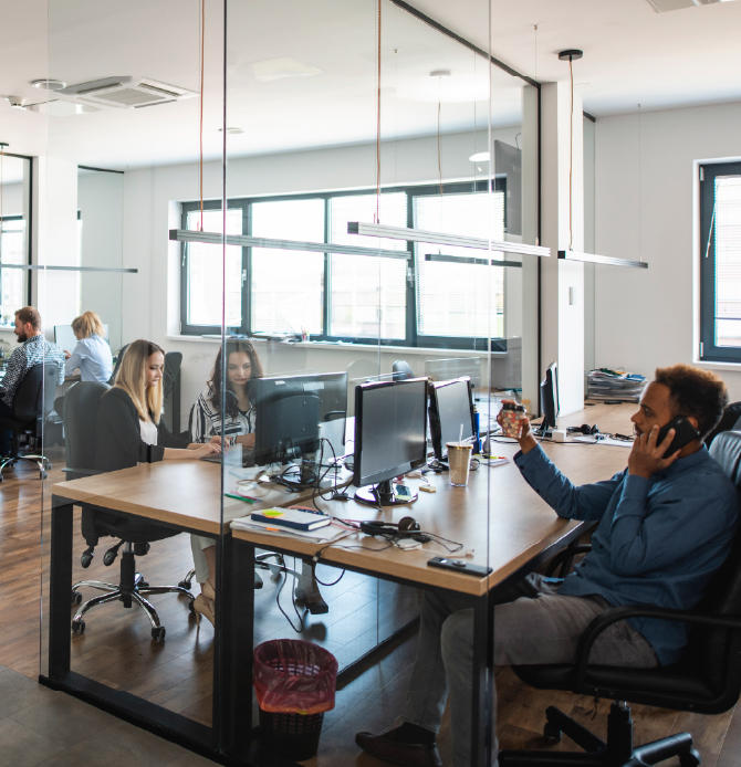 A modern office space with people working at desks and large windows in the background