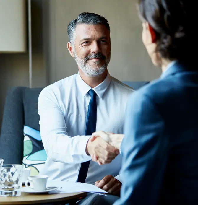 Two people shaking hands in a professional setting with a table between them
