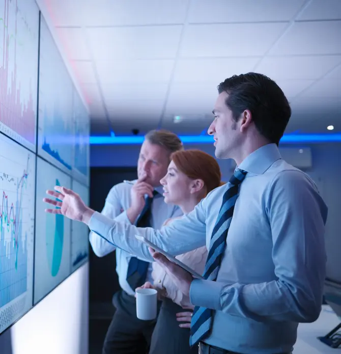 Three professionals analyzing graphs on large digital screens in an office