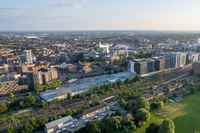 Aerial view of a city with modern buildings, railway lines, and green spaces.