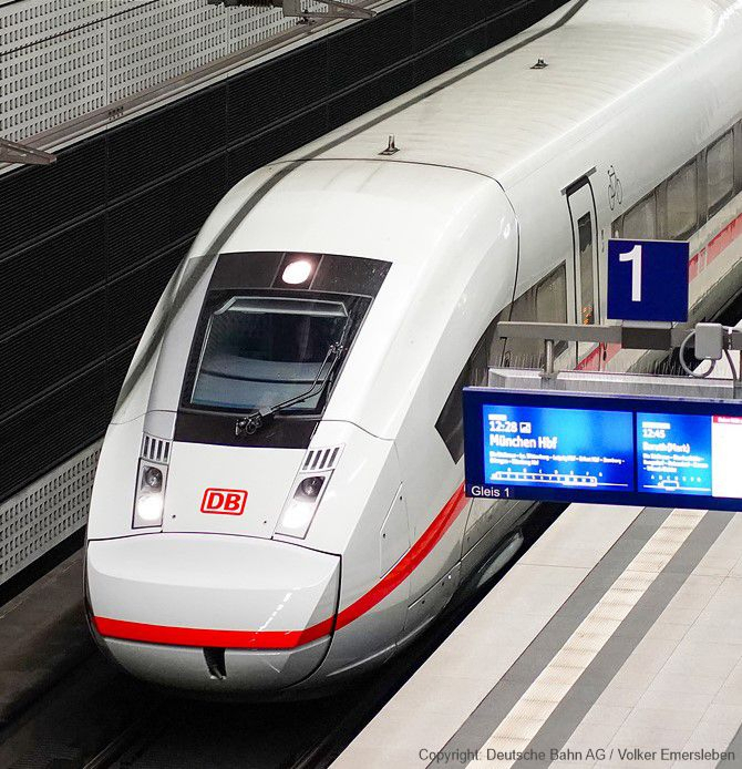 A modern white high-speed train at a station platform with an electronic display board